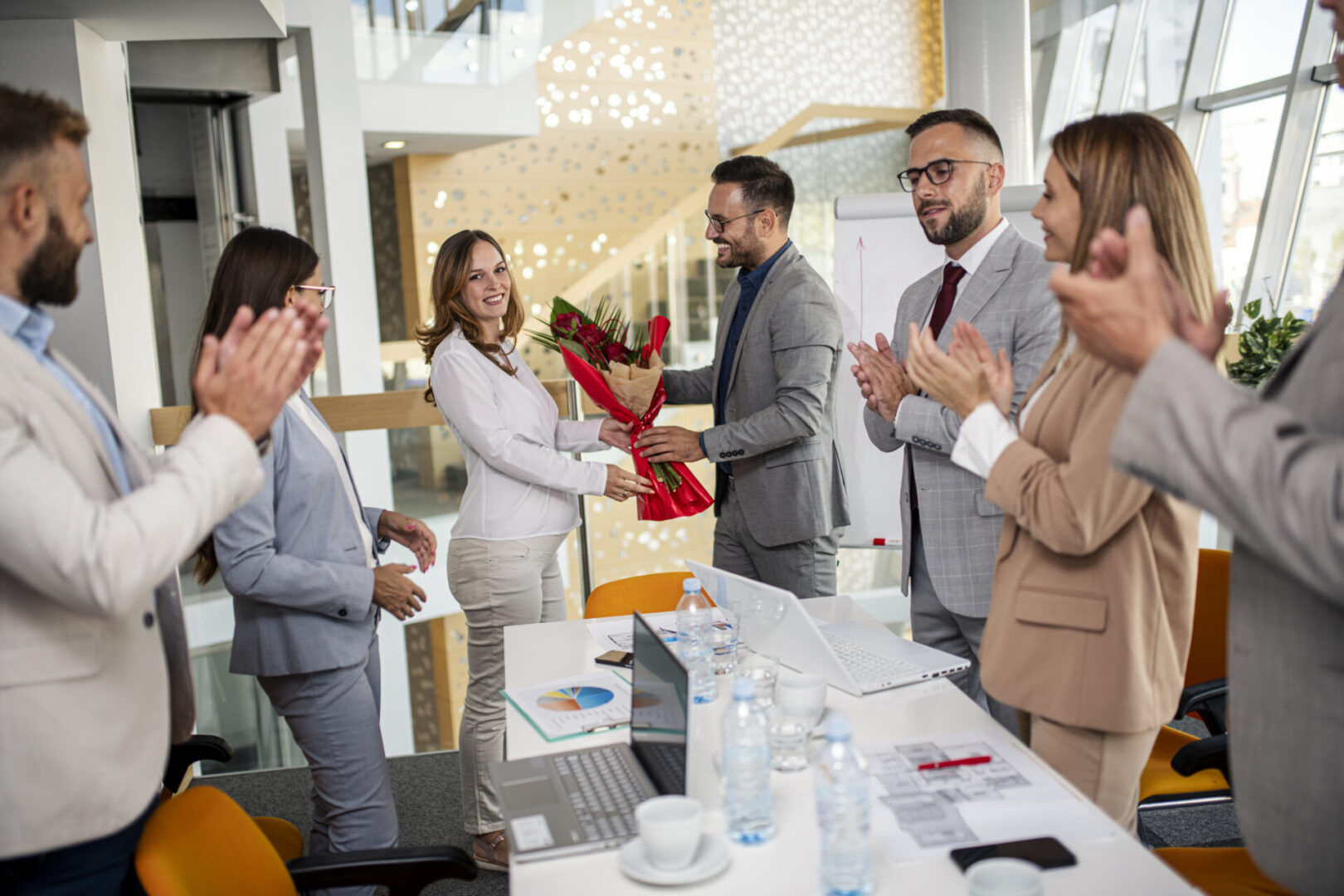 Office celebration with colleagues applauding and flowers.